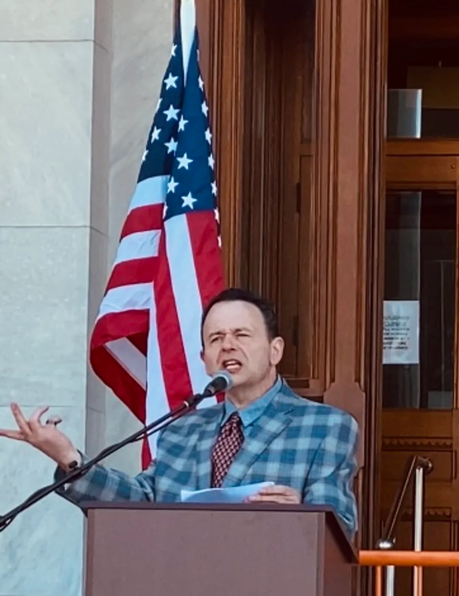 Dan Newmyer speaking at a podium in front of an American flag